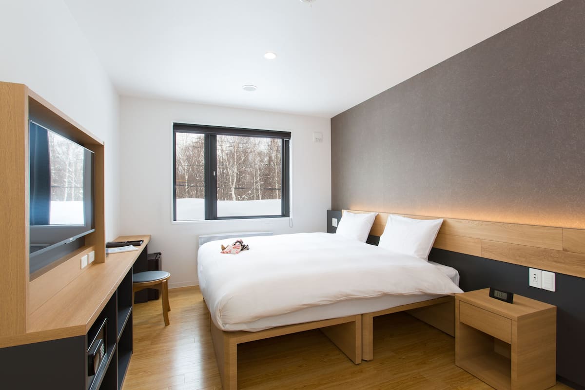 Habitación de hotel moderna con una cama grande, un escritorio y ventana con vistas a árboles.