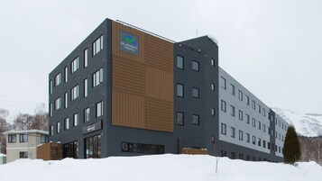 Un hôtel moderne, avec un logo bien visible sur la façade, de nombreuses fenêtres et un sol recouvert de neige.