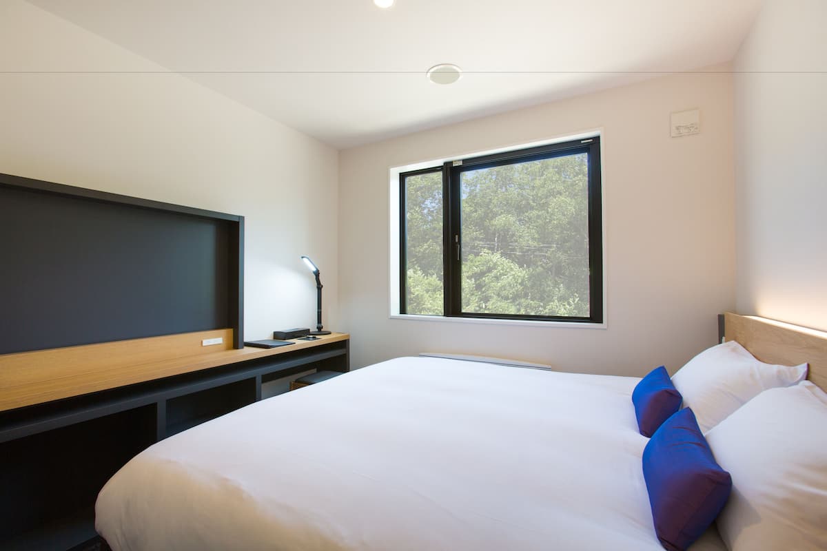 Un dormitorio moderno con una cama grande, un escritorio, un televisor de pantalla plana y un ventanal con vistas a árboles.
