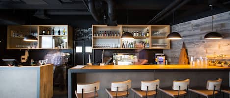 A modern bar area with wooden shelves, bar stools, and overhead lighting.
