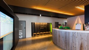 Un área de recepción moderna con un mostrador de madera, un espacio de estar con taburetes y una gran pantalla digital a la izquierda.