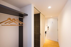 Um corredor com um porta-roupas de madeira, uma porta com puxador e uma parede revestida de azulejos.