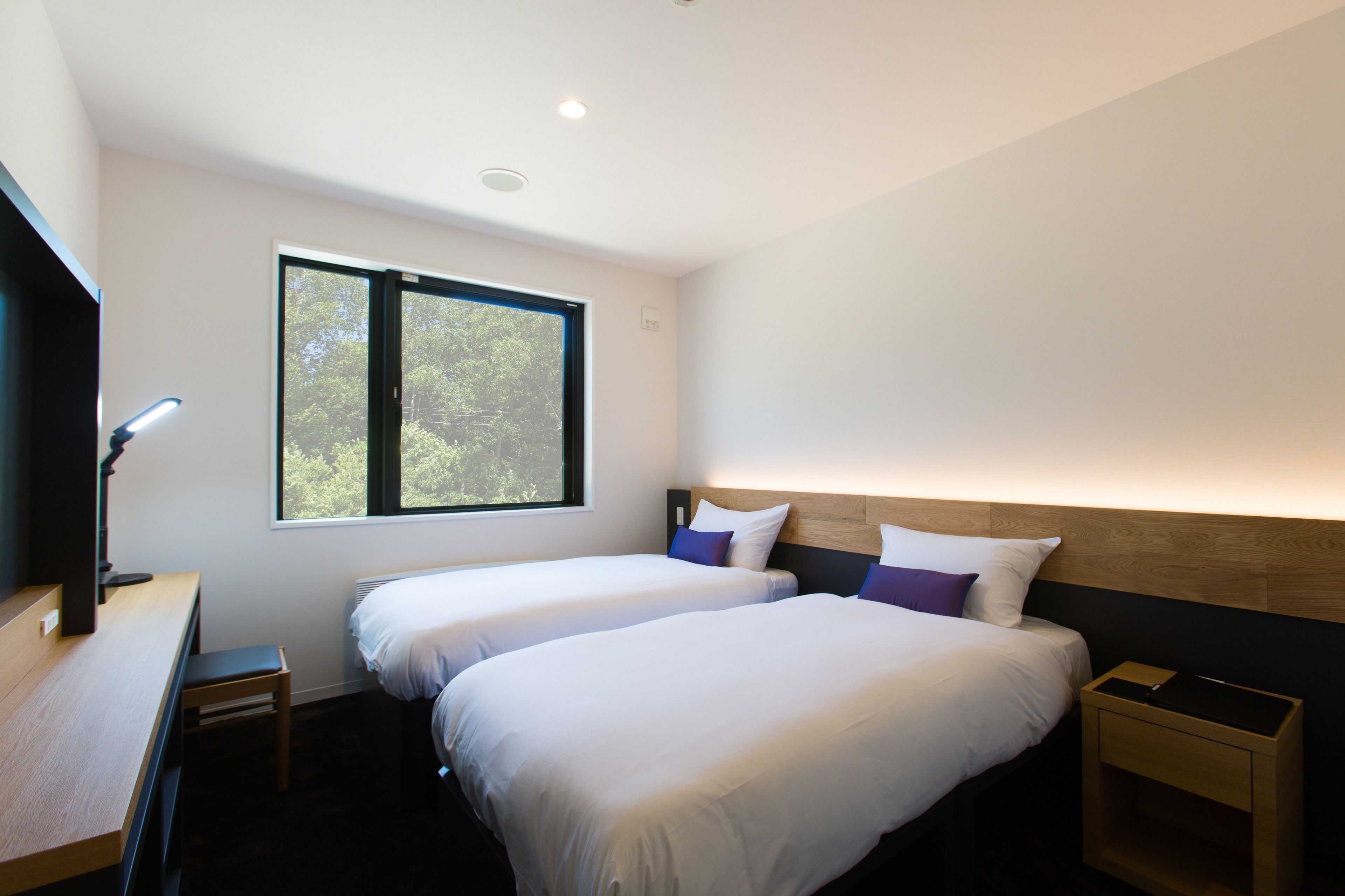 Habitación de hotel moderna con dos camas, un escritorio y ventana con vista a árboles.