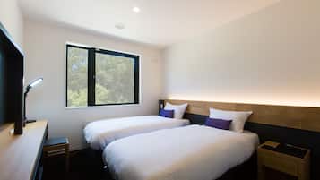A modern hotel room with two beds, a desk, and a window providing a view of trees.