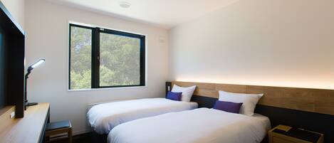 A modern hotel room with two beds, a desk, and a window providing a view of trees.
