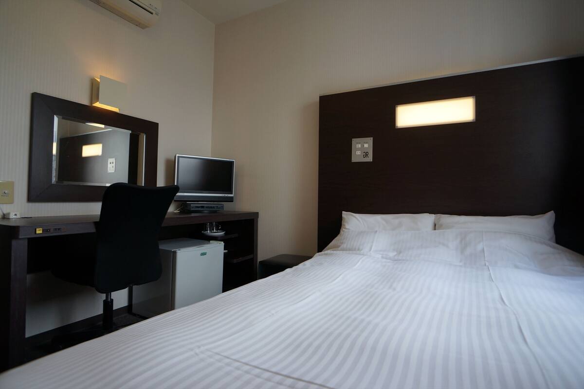 Een hotelkamer met een bed, een bureau met een computer, een stoel en een kleine koelkast.