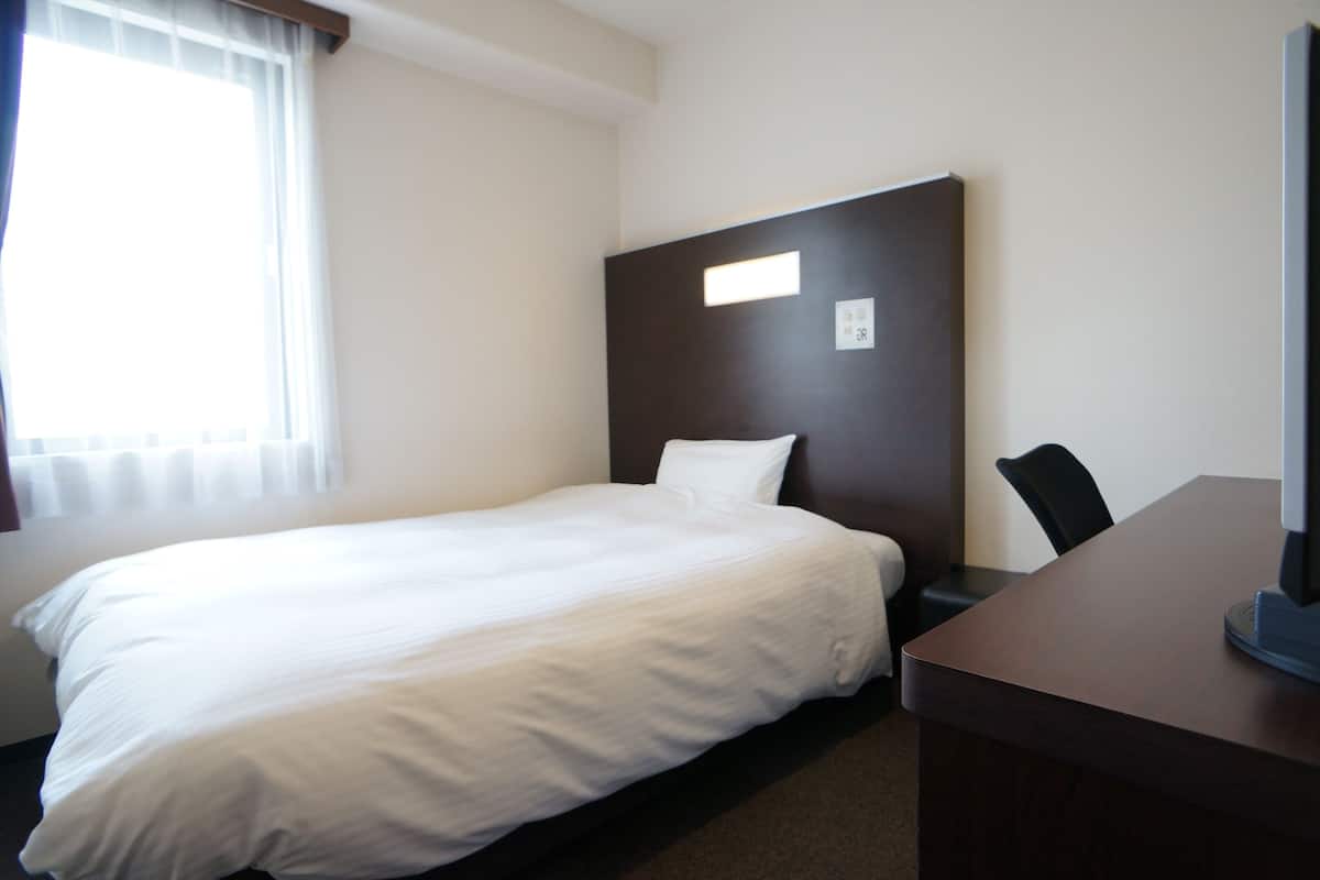 Een hotelkamer met een eenpersoonsbed, een bureau en een stoel.