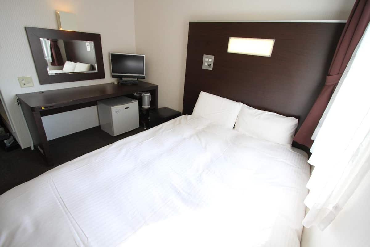 Een hotelkamer met een bed, een bureau met een computer, een televisie en een kleine koelkast.