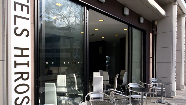 A hotel entrance with glass doors, outdoor seating with metal chairs, and a sign reading "HIROSHIMA". - Green Rich Hotel Hiroshima Shinkansenguchi (Artificial hot spring Futamata Yunohana) (Hiroshima)