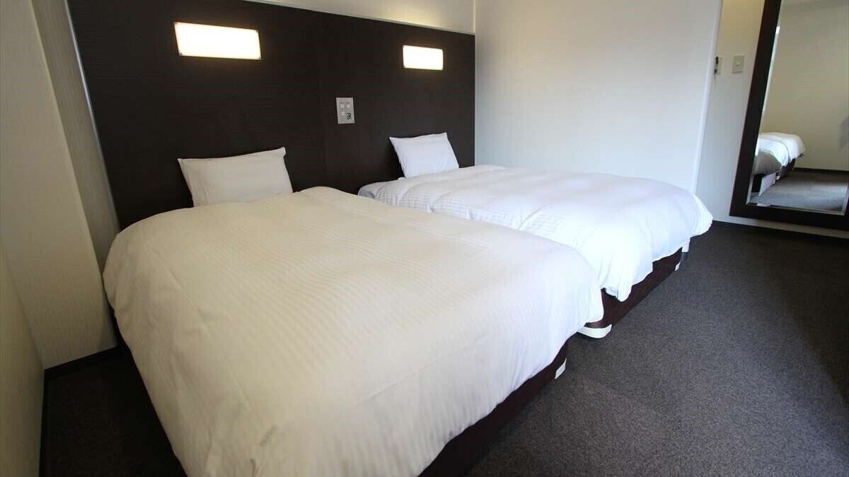 A hotel room with two beds, dark headboard, and a large mirror.