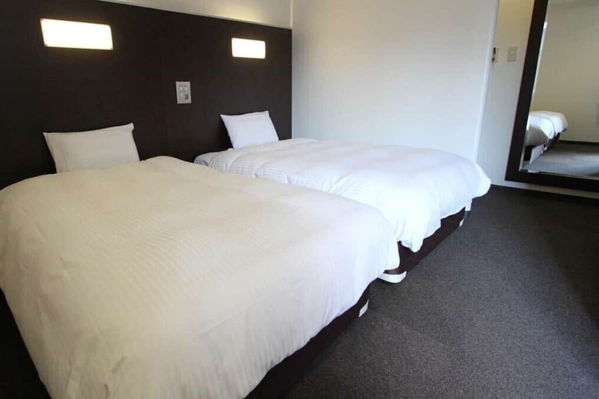 A hotel room with two beds, dark headboard, and a large mirror.