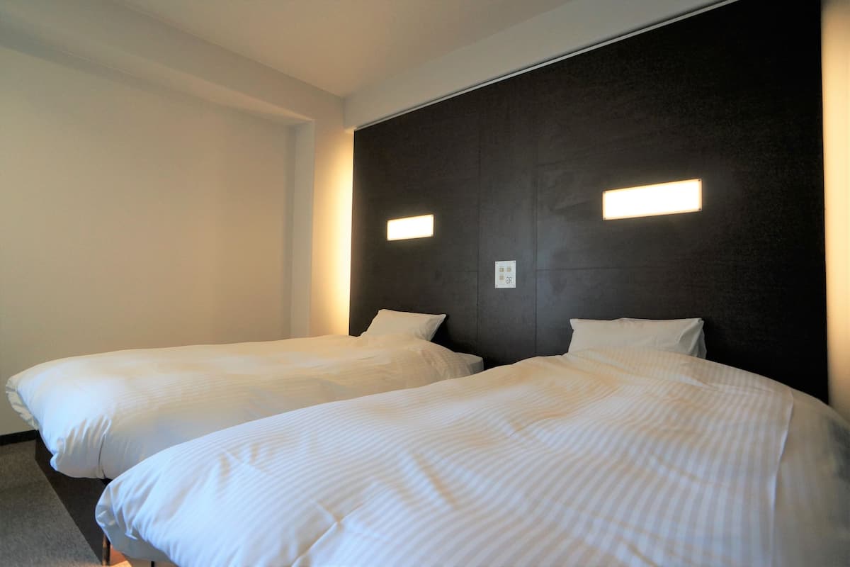Twee eenpersoonsbedden met witte beddengoed in een kamer met een donkere hoofdbord en twee wandlampen.