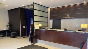 A modern hotel reception area with a dark wood reception desk, a black leather ottoman, and a blue accent wall. - Green Rich Hotel Hiroshima Shinkansenguchi (Artificial hot spring Futamata Yunohana) (Hiroshima)