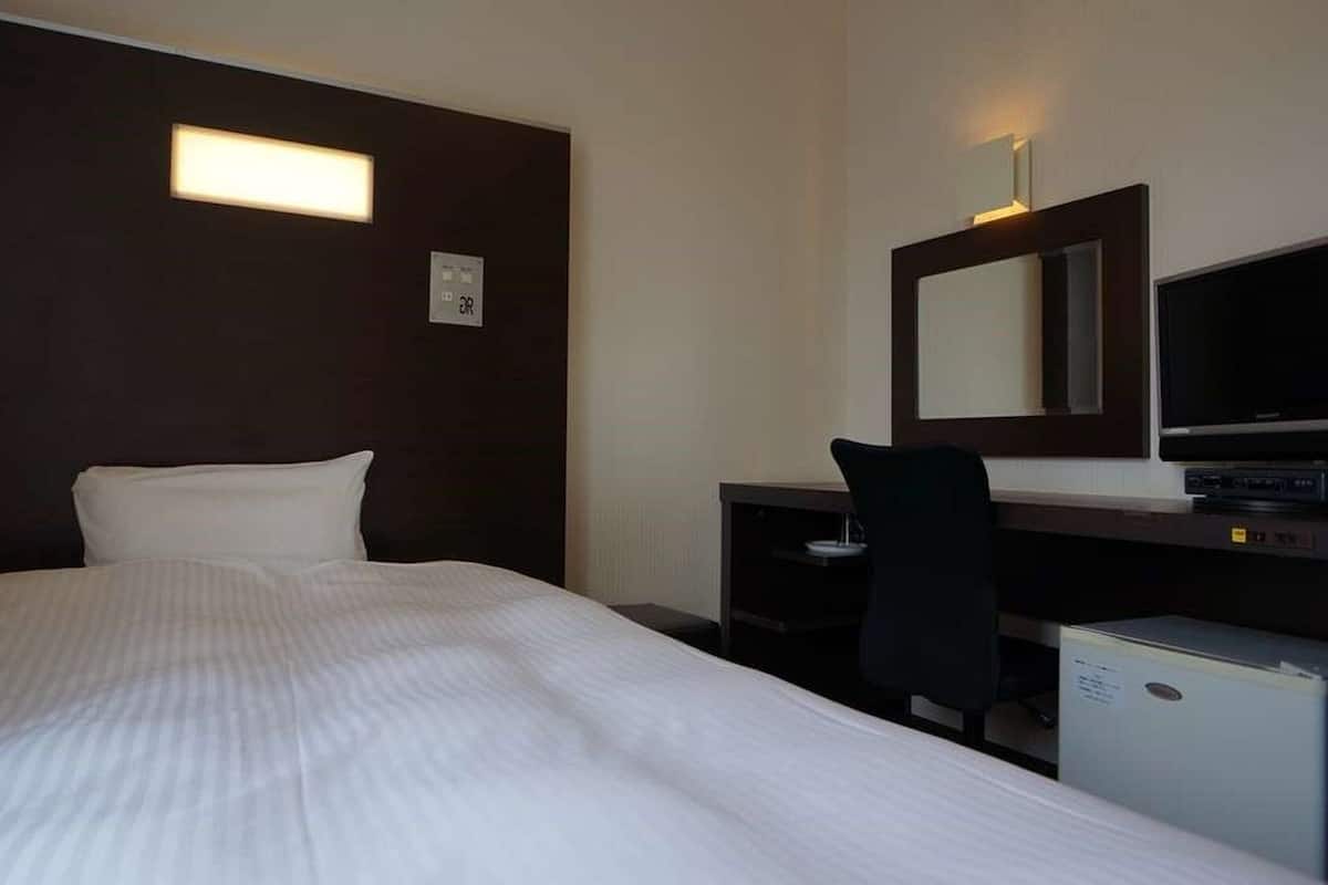 A hotel room with a bed, a desk, a chair, a television, and a small refrigerator.