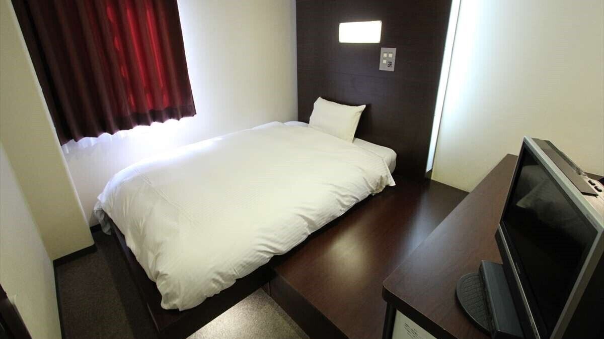 A hotel room with a bed, a television, and a small desk.