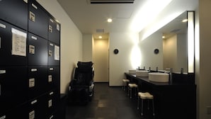 A hotel bathroom with lockers, a massage chair, and a vanity with two sinks.