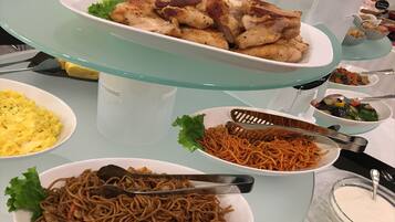 Una mesa de buffet con diversos platos, incluyendo pollo frito, fideos, huevos revueltos y verduras.