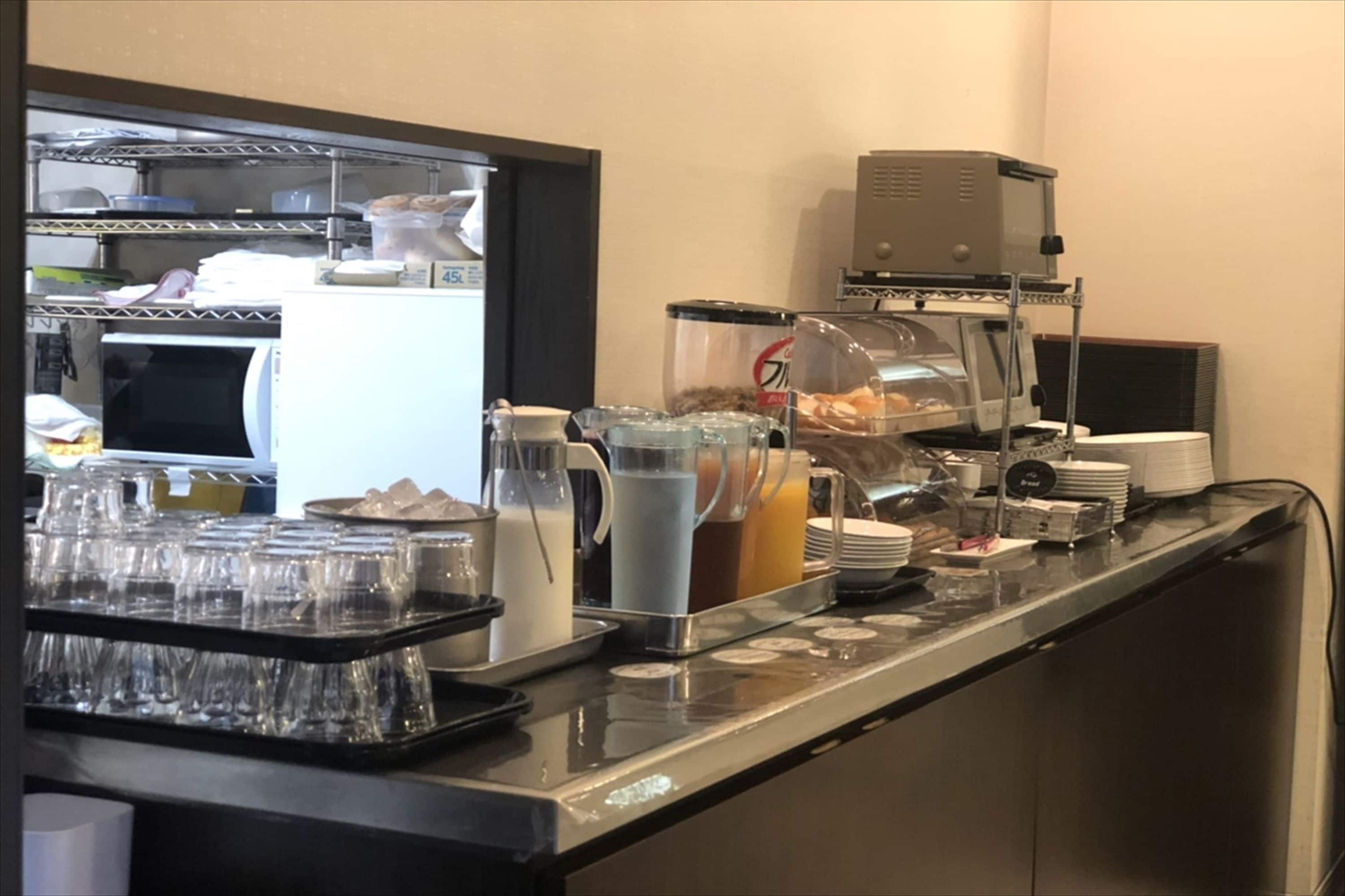 A buffet setup with various food and drink containers, a coffee machine, and a microwave.