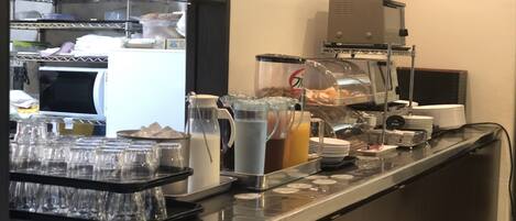 Een buffetopstelling met diverse bakken voor eten en drinken, een koffieapparaat en een magnetron.
