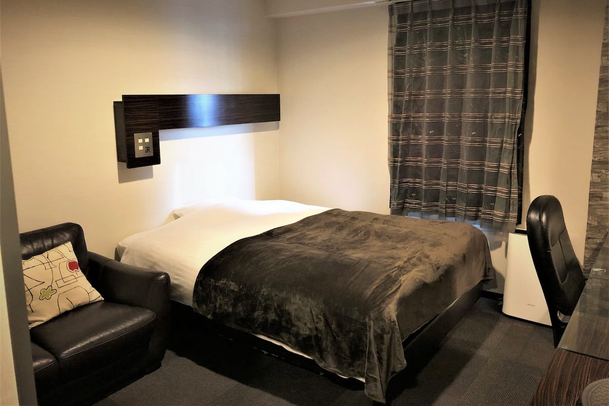 Une chambre d’hôtel avec un lit, un bureau, une chaise et une fenêtre avec des rideaux.