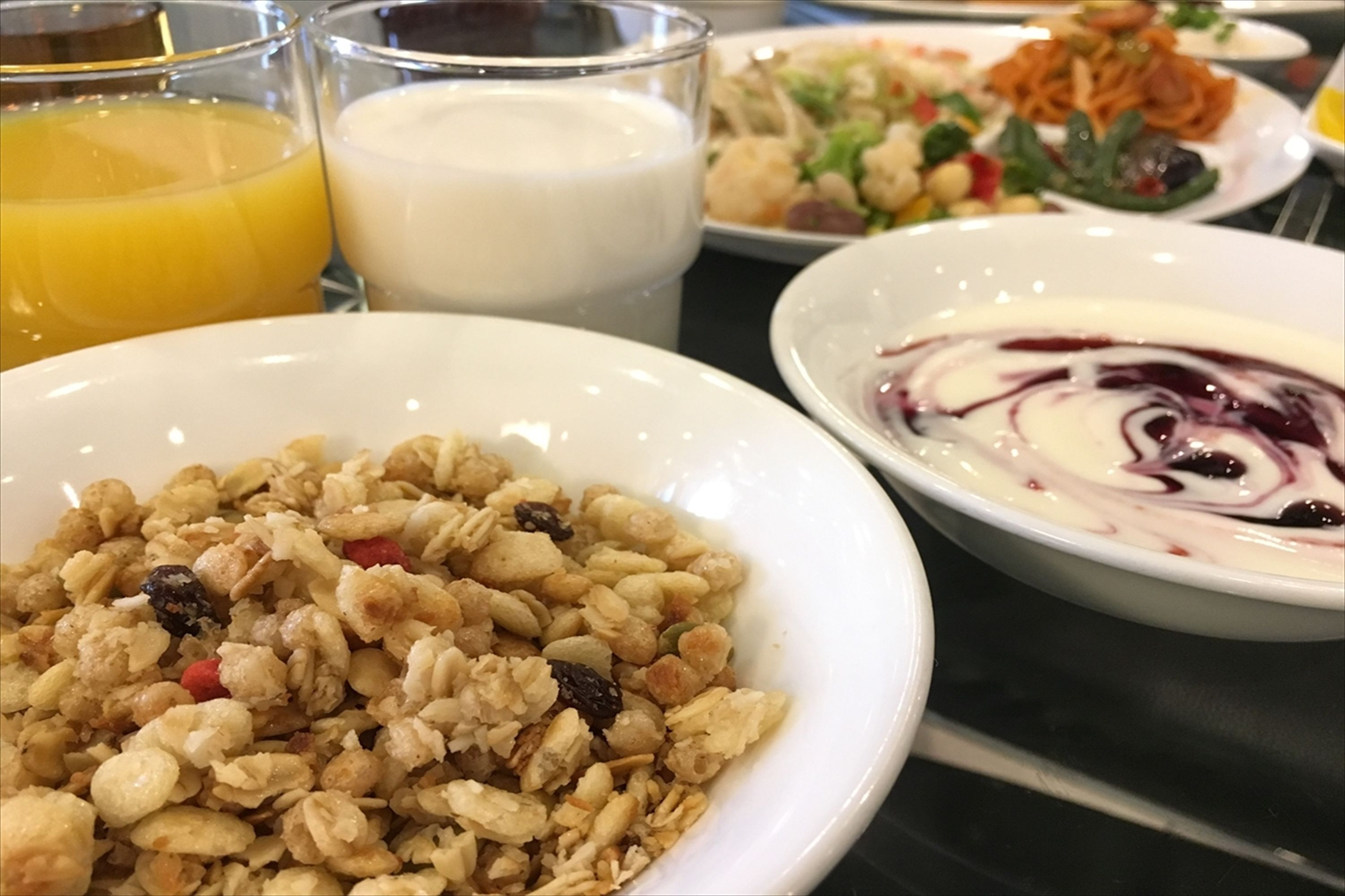 A breakfast setting with a bowl of granola, a bowl of yogurt with berries, a glass of orange juice, and a plate of salad.
