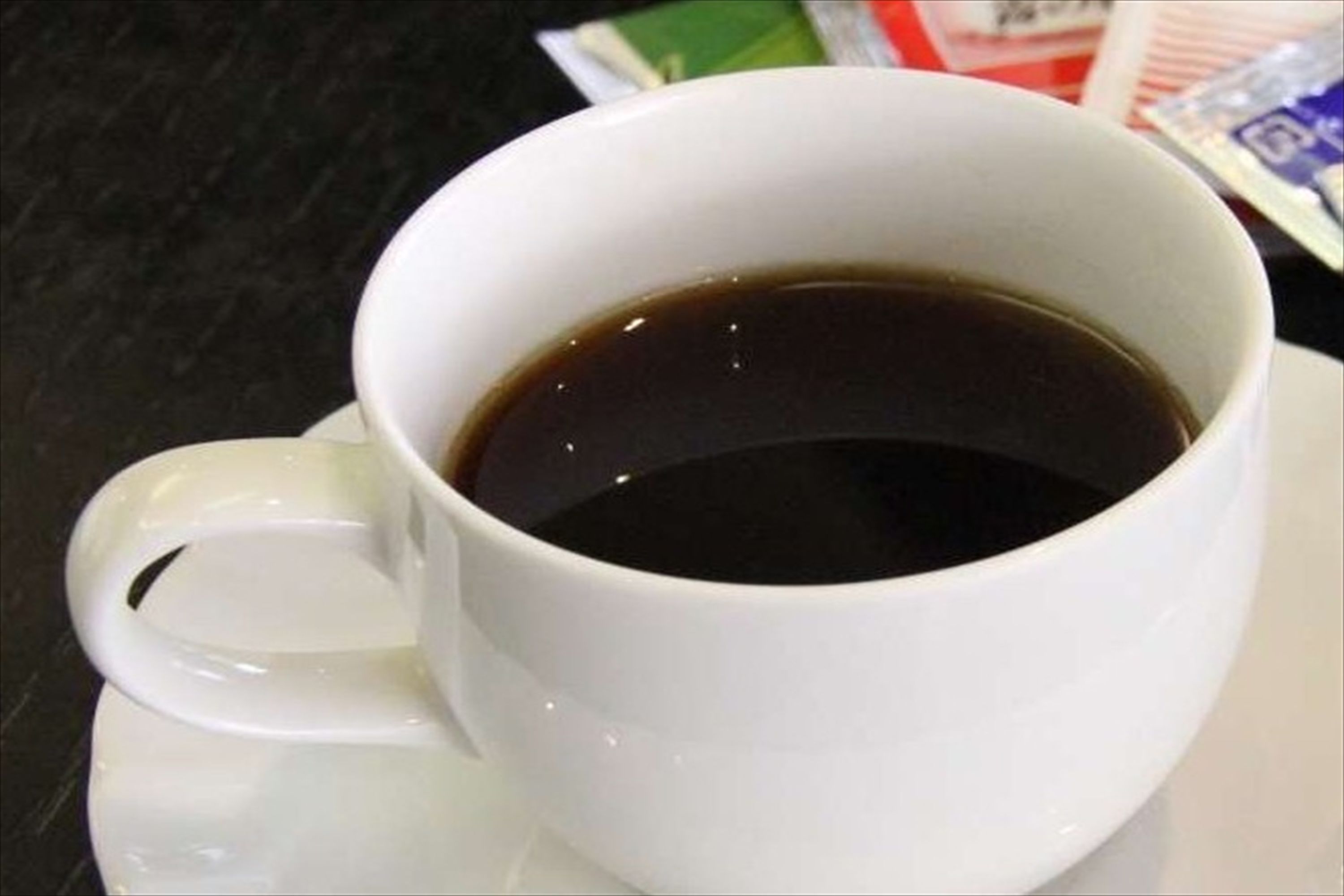 A white cup filled with a dark liquid, likely coffee, on a white saucer.