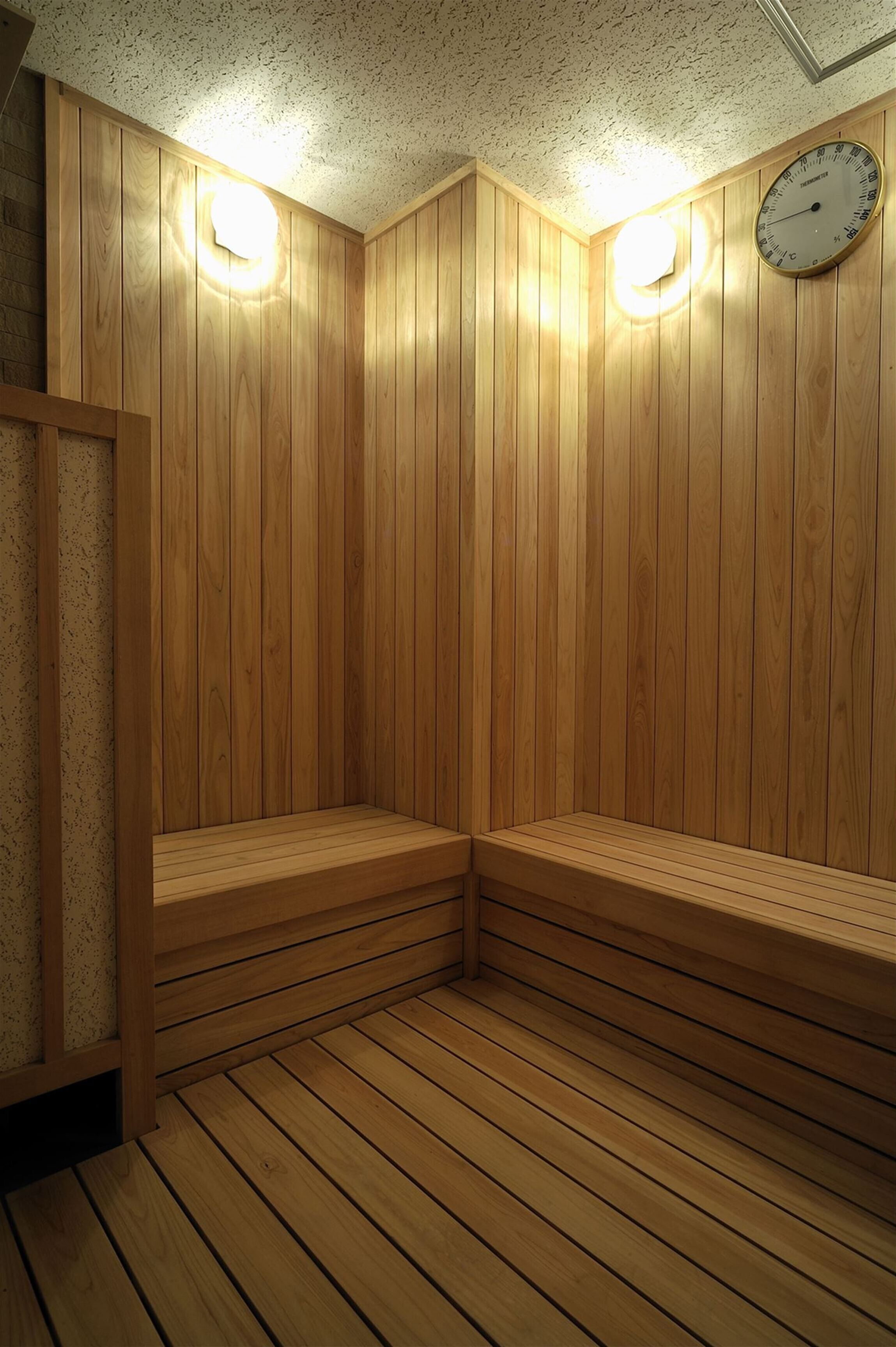Una sauna con paredes y bancos de madera, dos luces fijadas en la pared y un reloj.