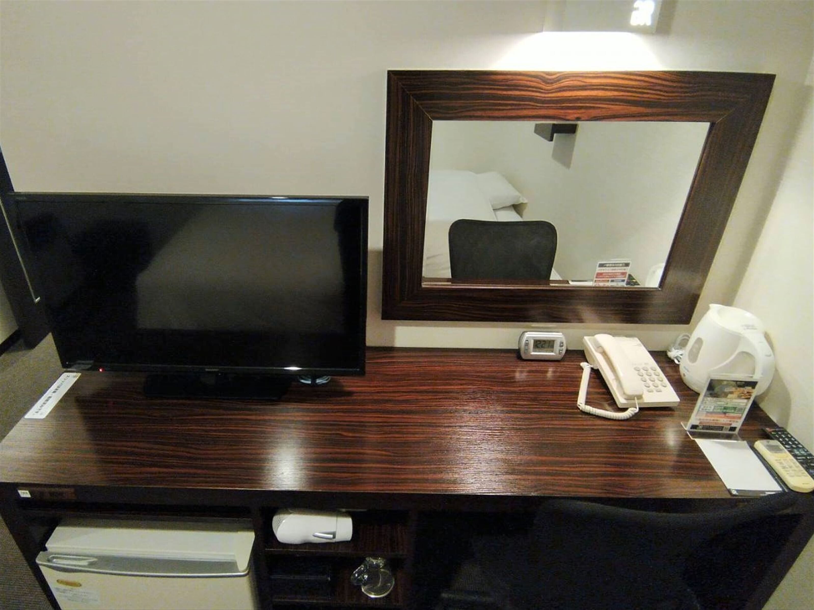 A hotel room with a wooden desk, a flat-screen TV, a telephone, a coffee maker, and a mirror.