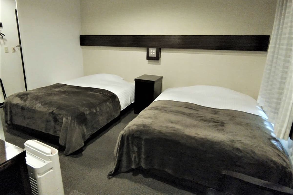 Een hotelkamer met twee enkele bedden, een klein nachtkastje, een verwarming en een wandlamp.