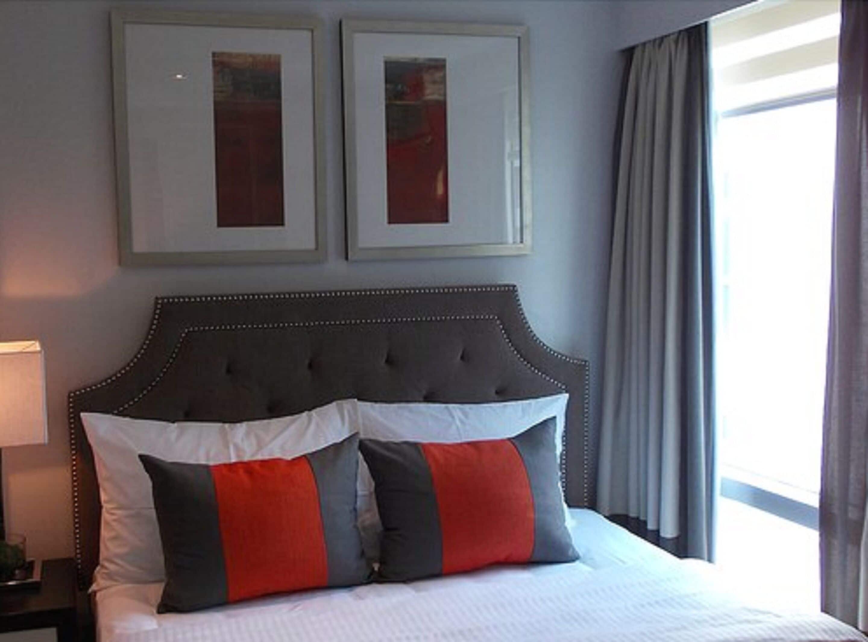A neatly made bed with a tufted headboard, two framed pictures on the wall, and a window with curtains.