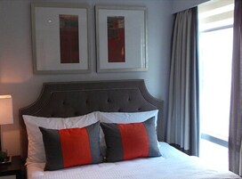 A neatly made bed with a tufted headboard, two framed pictures on the wall, and a window with curtains.