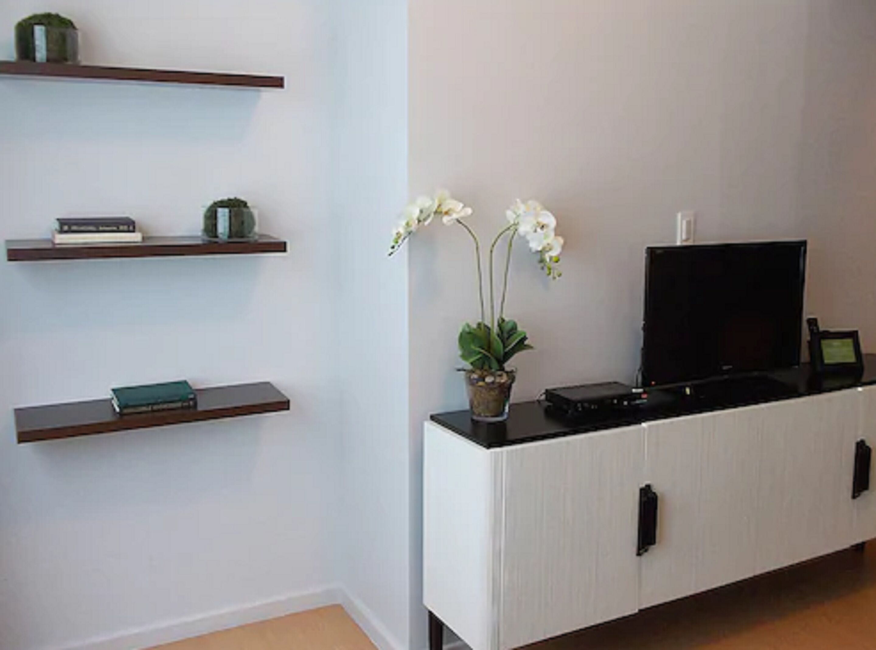 A living room with a white entertainment unit, a flat-screen TV, and a potted orchid.