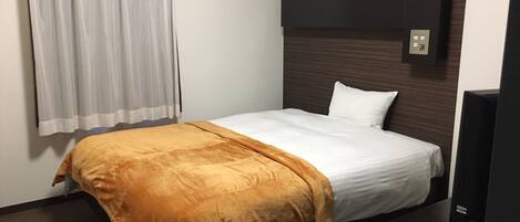 Ein Hotelzimmer mit einem Einzelbett, einem hölzernen Kopfteil, einem Fernseher und einem Fenster mit Vorhängen.