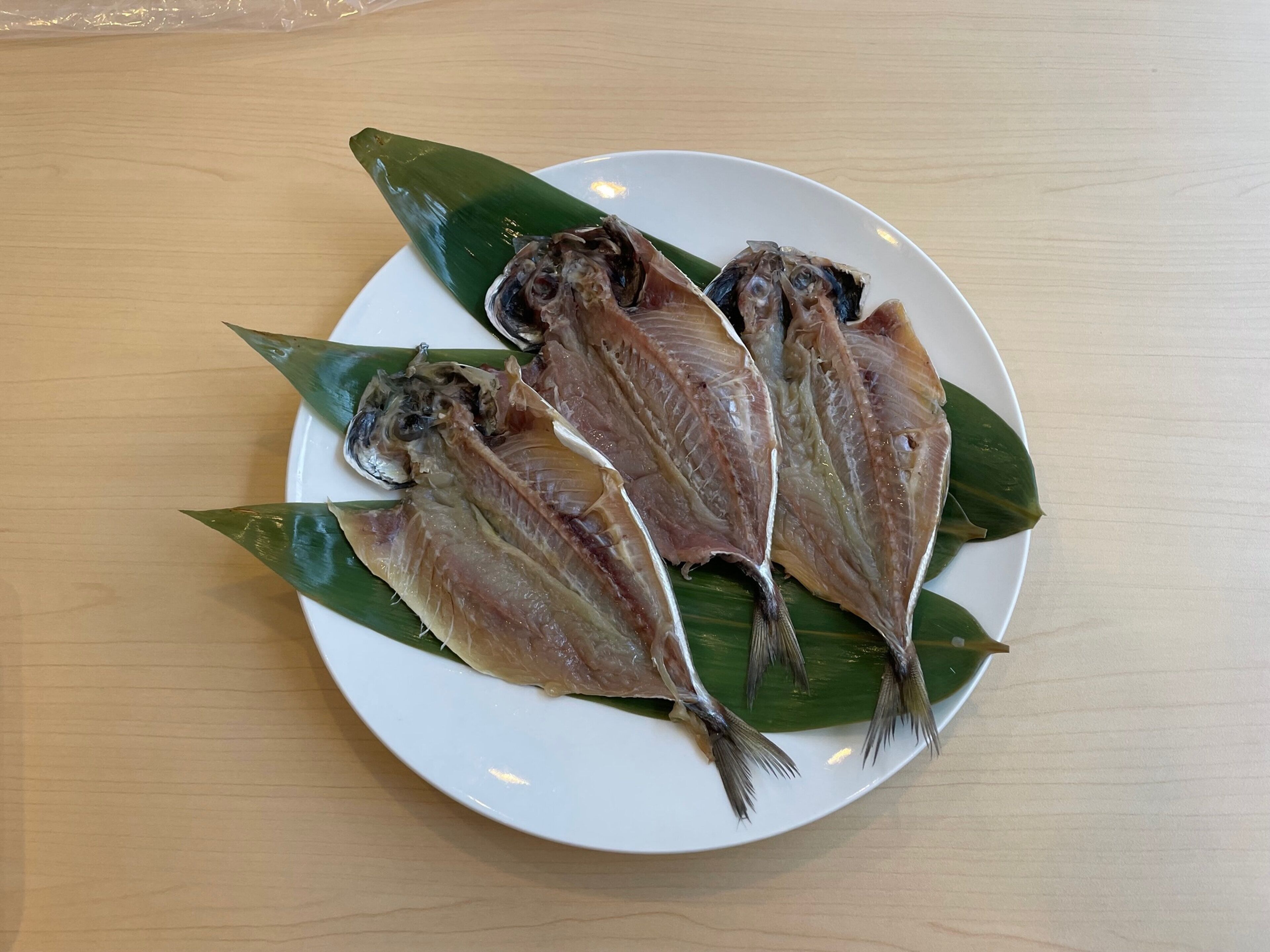A plate with three fish on a white plate, placed on a wooden table.