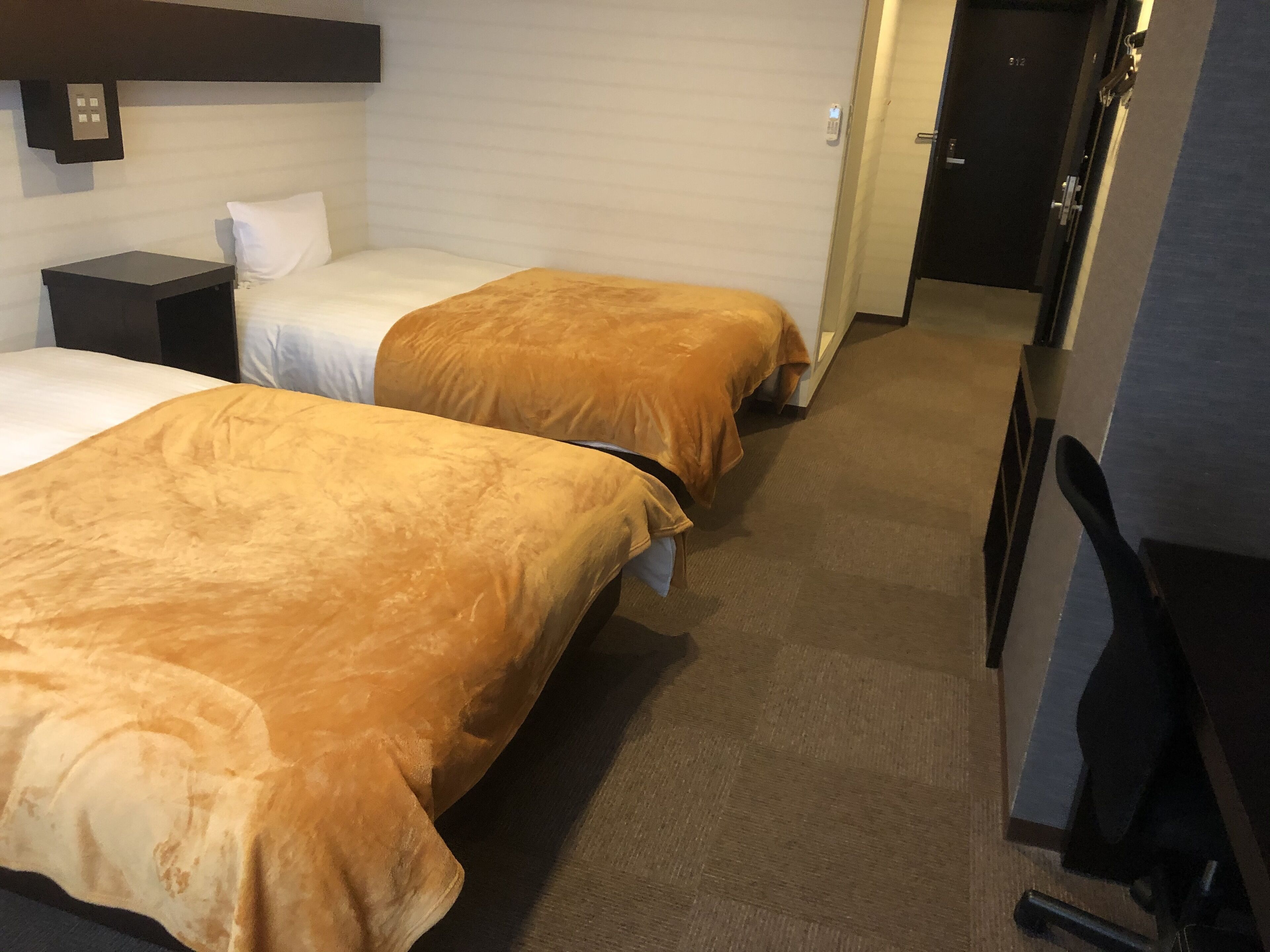 Habitación de hotel con dos camas, una mesita de noche, un escritorio y una puerta que da a otra habitación.