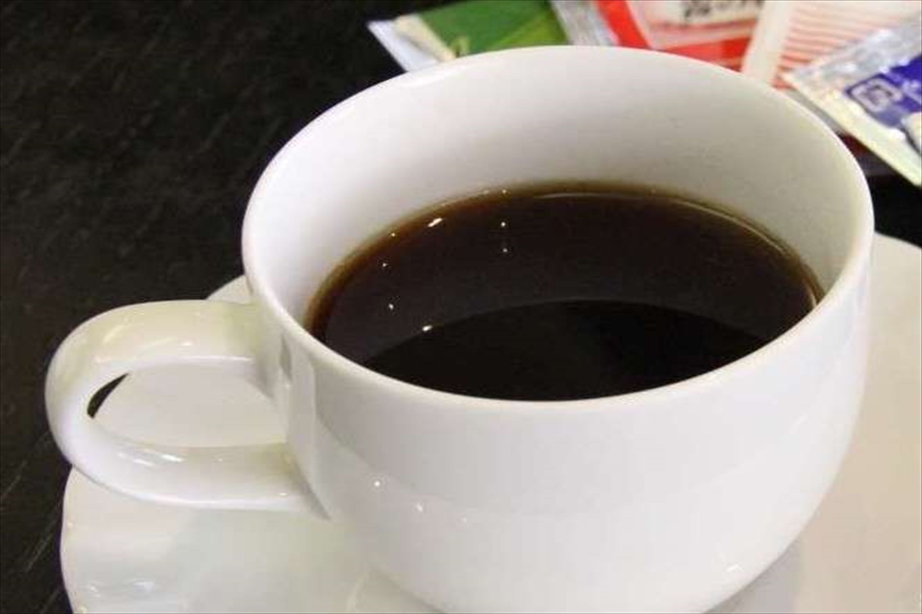Une tasse blanche remplie d’un liquide sombre, vraisemblablement du café, posée sur une soucoupe blanche.