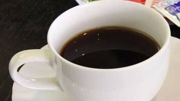 Une tasse blanche remplie d’un liquide sombre, vraisemblablement du café, posée sur une soucoupe blanche.