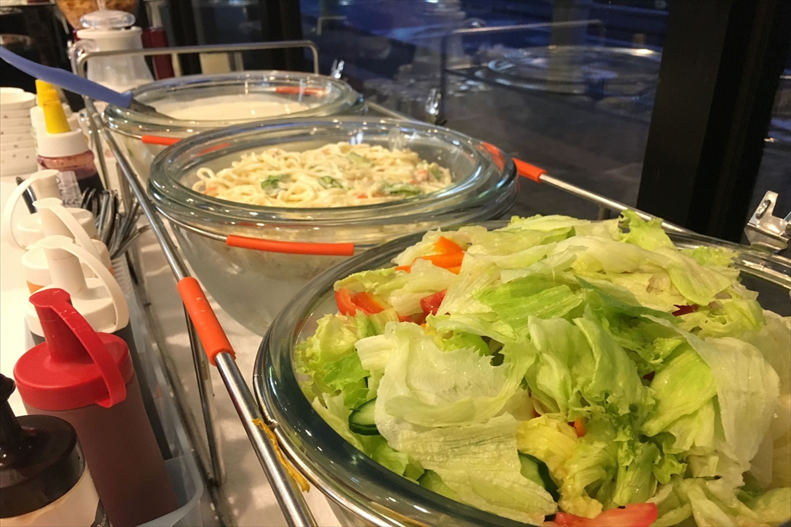 A buffet with various food items, including a salad and a pasta dish, and condiment dispensers.