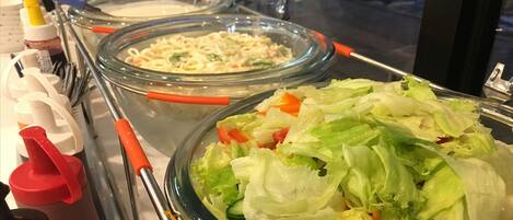A buffet with various food items, including a salad and a pasta dish, and condiment dispensers.