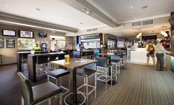 Un espace bar moderne avec des tabourets hauts, un comptoir où est présenté le menu, et un coin salon avec des tables et des chaises.