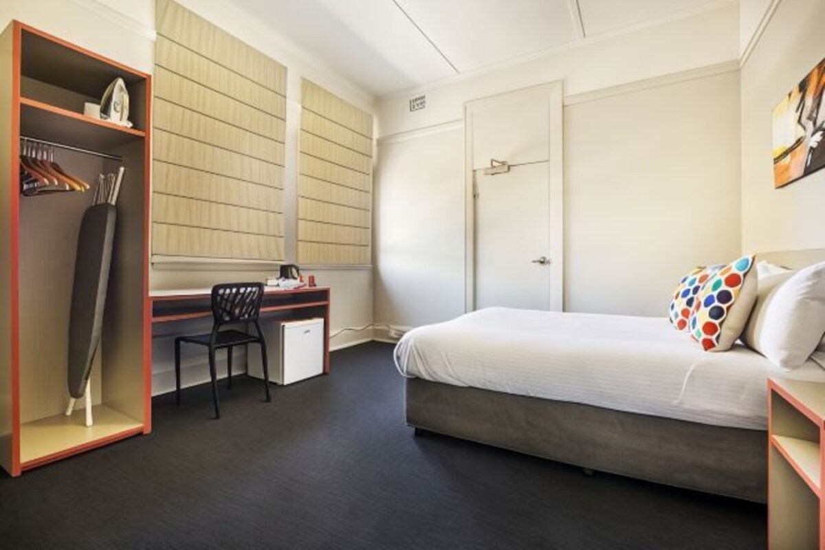 A bedroom with a bed, a desk, a chair, a wardrobe, and a small cabinet.