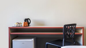 A compact workspace with a desk, a chair, a coffee maker, and a small refrigerator. - Granville Hotel (Granville)