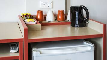 A kitchenette with a refrigerator, coffee maker, and various mugs.