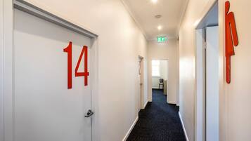 A hallway with white walls, black carpet, and doors marked with red numbers.