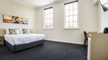 A hotel room with a bed, two windows, a desk, and a chair.