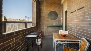A small, enclosed outdoor area with a brick wall, a round table with chairs, a gas stove, and a window overlooking a cityscape. - Granville Hotel (Granville)