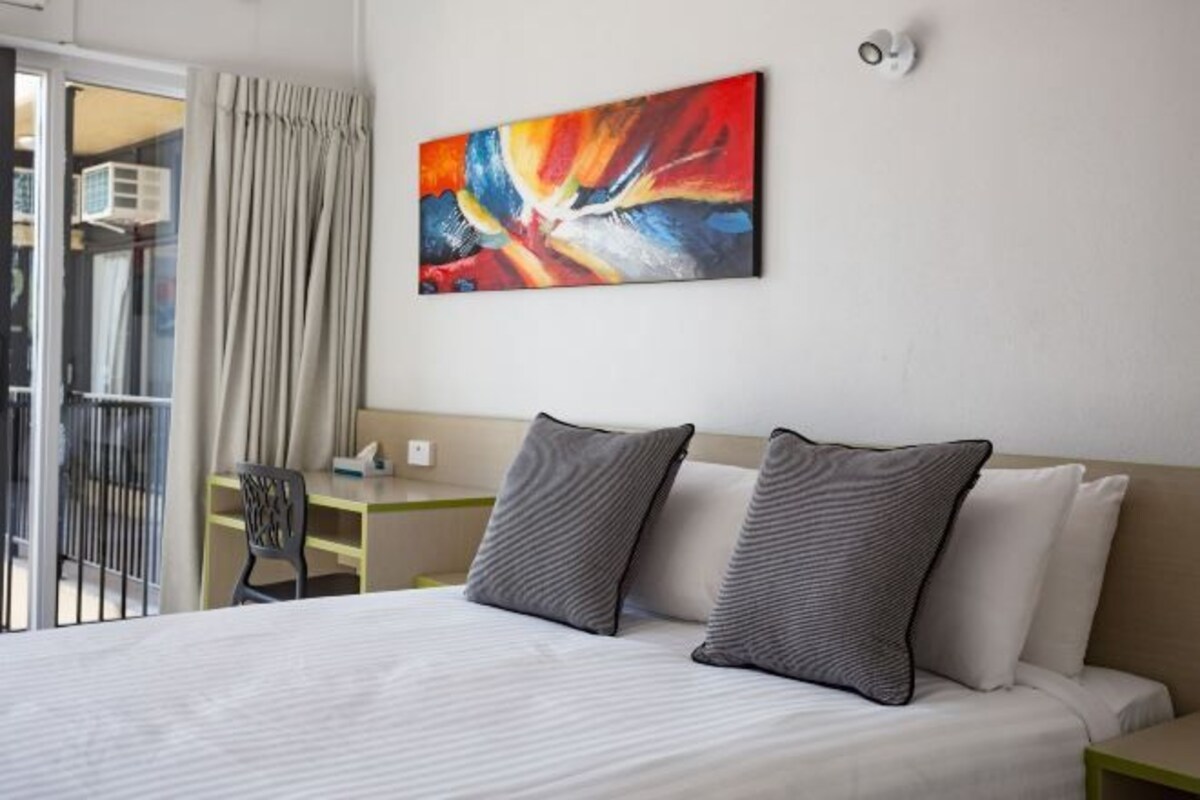 A hotel room with a bed, two pillows, a painting on the wall, and a window with curtains.