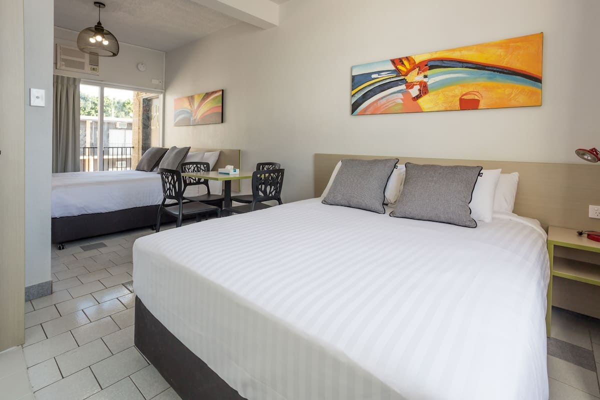 A hotel room with two beds, a desk, and a chair. There is a painting on the wall and a window with curtains.