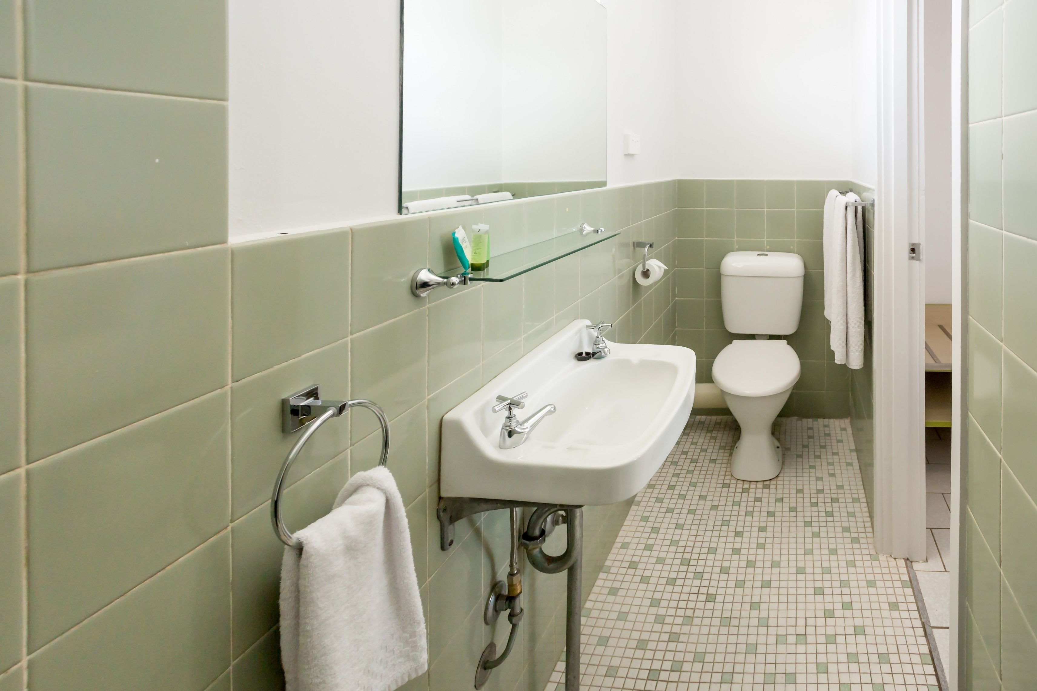 A bathroom with a white sink, a toilet, and a glass shelf.