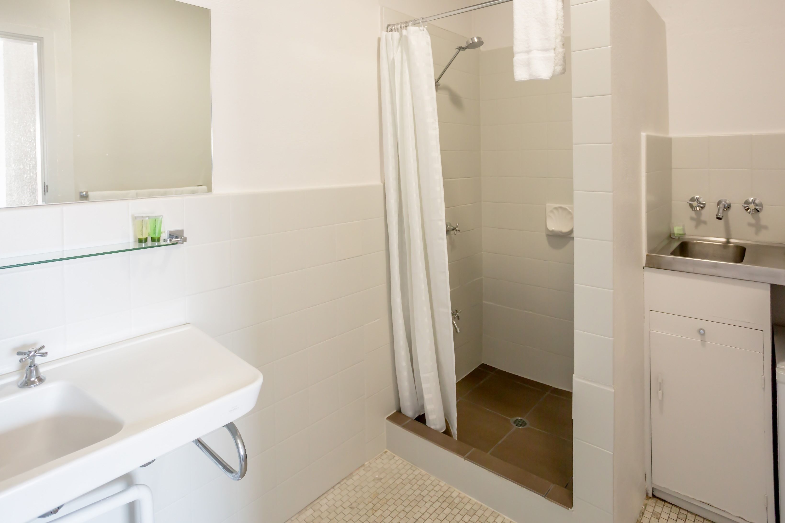 Un bany amb un lavabo blanc, una dutxa amb cortina i un mirall sobre el lavabo.